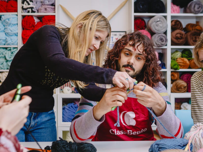 A man instructed by his teacher at a crochet class